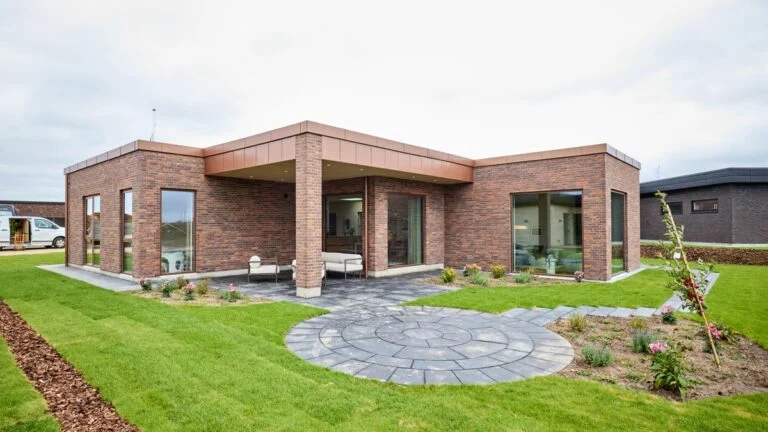 Lokalplanen i Margrethehøj åbner for en bred vifte af arkitektoniske muligheder. Her er en moderne HusCompagniet-villa med fladt tag, overdækket terrasse og varme teglsten, der falder naturligt ind i de grønne omgivelser.